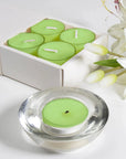 Close-up view of a green lily scented tealight candle sitting inside its heavy decorative glass holder, with the white gift box in the background.