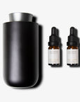 A dark gun metal waterless nebulizing diffuser standing next to two amber glass essential oil dropper bottles with black caps.