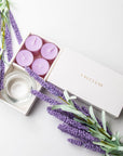 Top-down minimalist flat lay of the open lavender tealight candle set beautifully decorated with purple lavender faux stems on a seamless white backdrop.