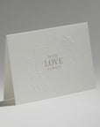 An elegant, freestanding white love card showcasing a delicate debossed floral motif framing the central typography.