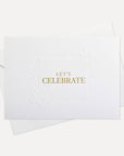 Front flat lay view of a minimalist luxury white celebration card featuring elegant gold text reading Let's Celebrate, displayed with its matching white envelope.