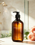 Vaucluse Lumière de Rose body wash placed on a bathroom counter next to fresh pink roses.