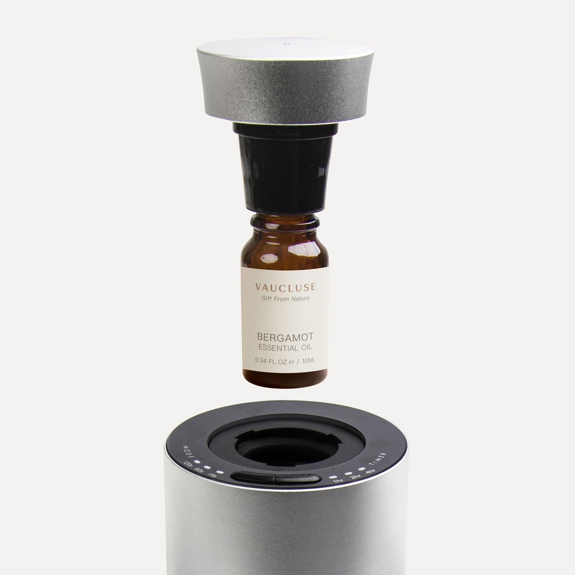 An instructional close-up showing a 10ml Vaucluse bergamot essential oil bottle screwing into a black nozzle mechanism above a silver waterless diffuser.