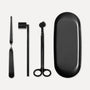 Matte black candle care accessory set featuring a wick trimmer, candle snuffer, wick dipper, and matching oval tray on a clean white background.