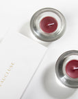A premium white Vaucluse 16-pack box sliding open to reveal the top tier of deep purple blackberry tealight candles, elegantly styled with rich dark berries.