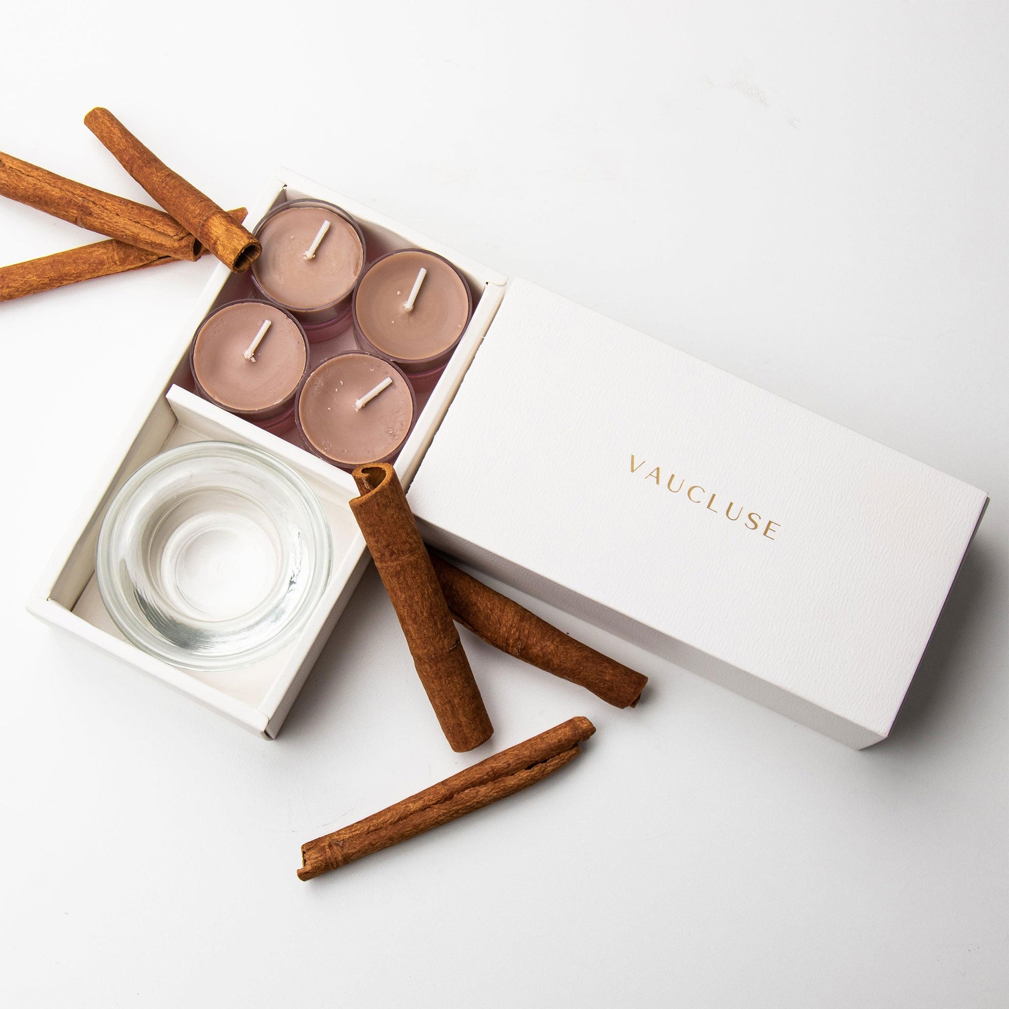 Top-down minimalist flat lay of the open cinnamon tealight candle set styled beautifully with raw cinnamon sticks on a seamless white surface.