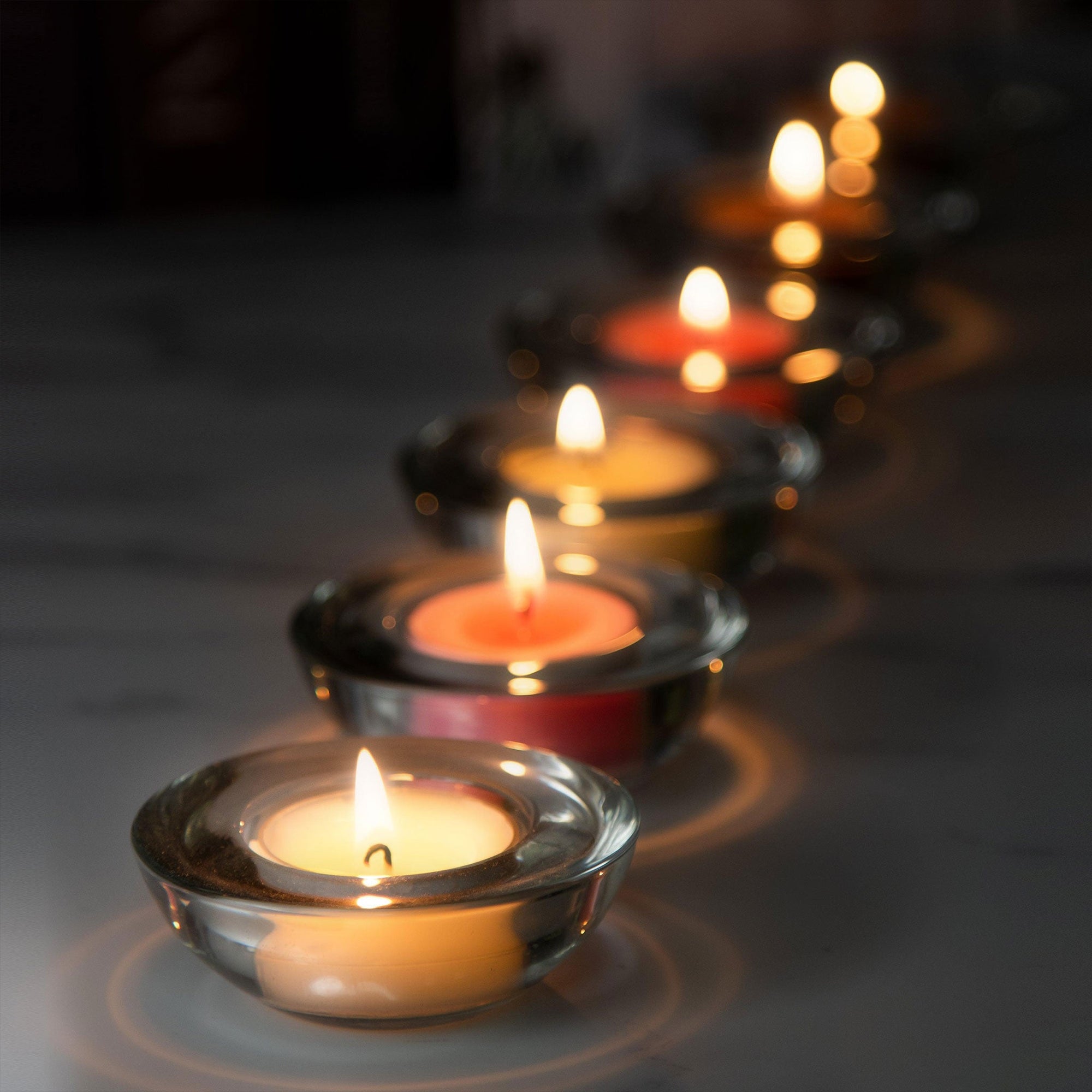 A sequential row of lit tealight candles in clear glass decorative holders fading out into a warm, soft golden bokeh background.