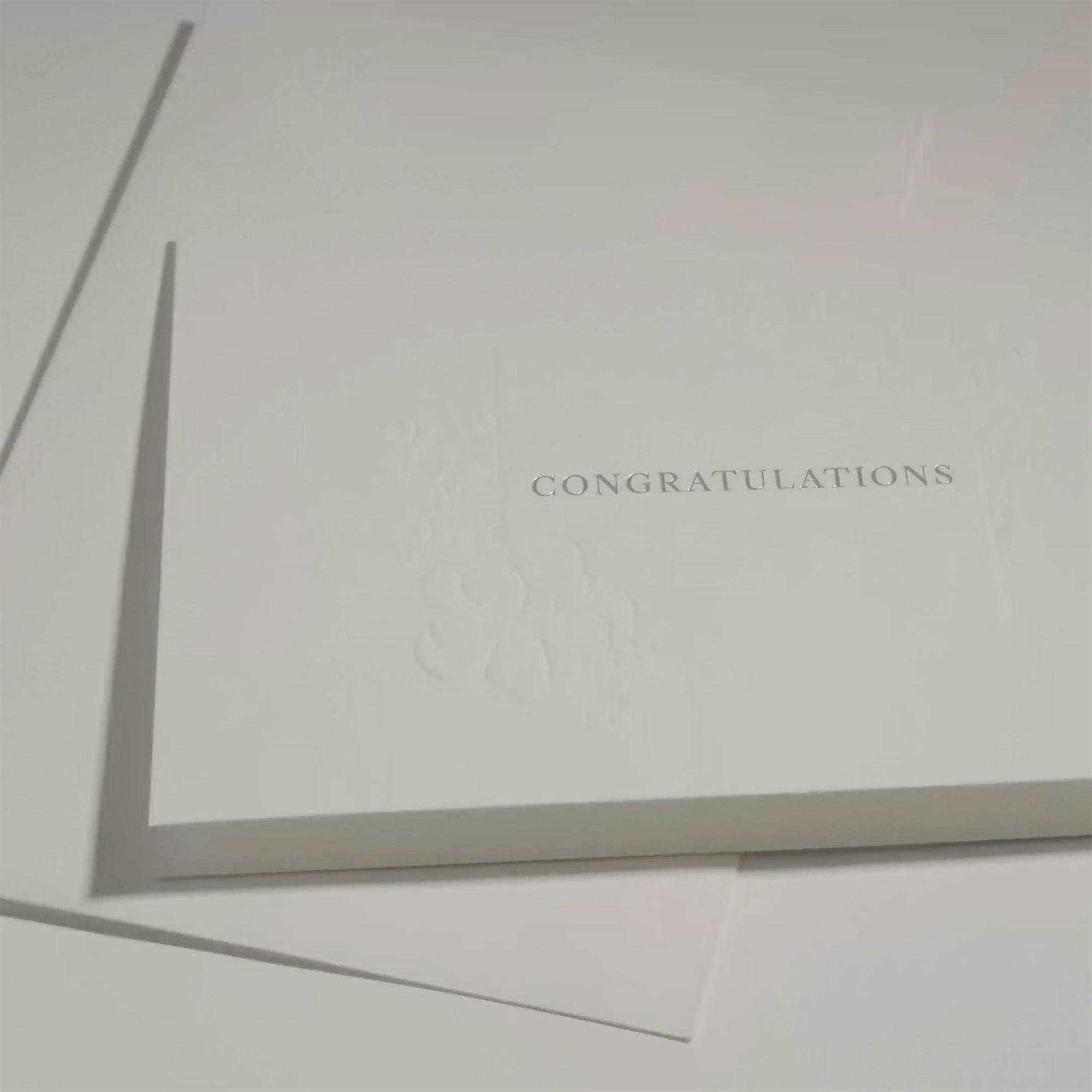 Side angle close-up emphasizing the crisp typography and premium embossed floral framework on a luxury wedding or corporate congratulations card.