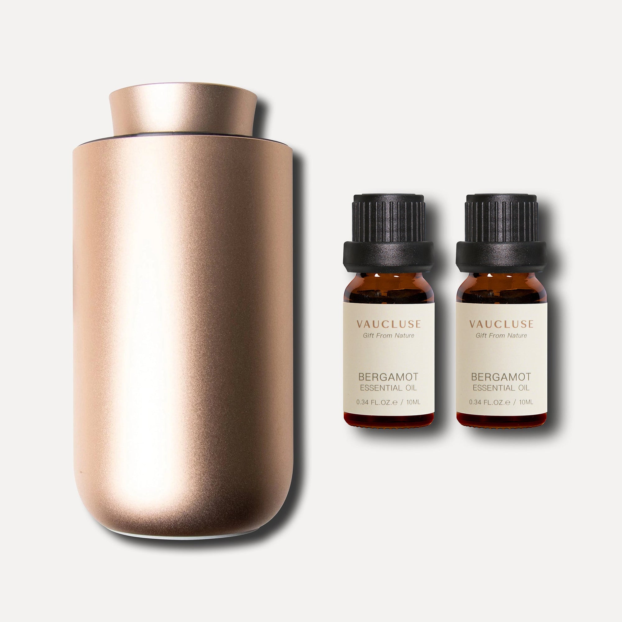 A sleek rose gold waterless nebulizing aroma diffuser displayed with two 10ml Vaucluse amber bottles of bergamot essential oil.