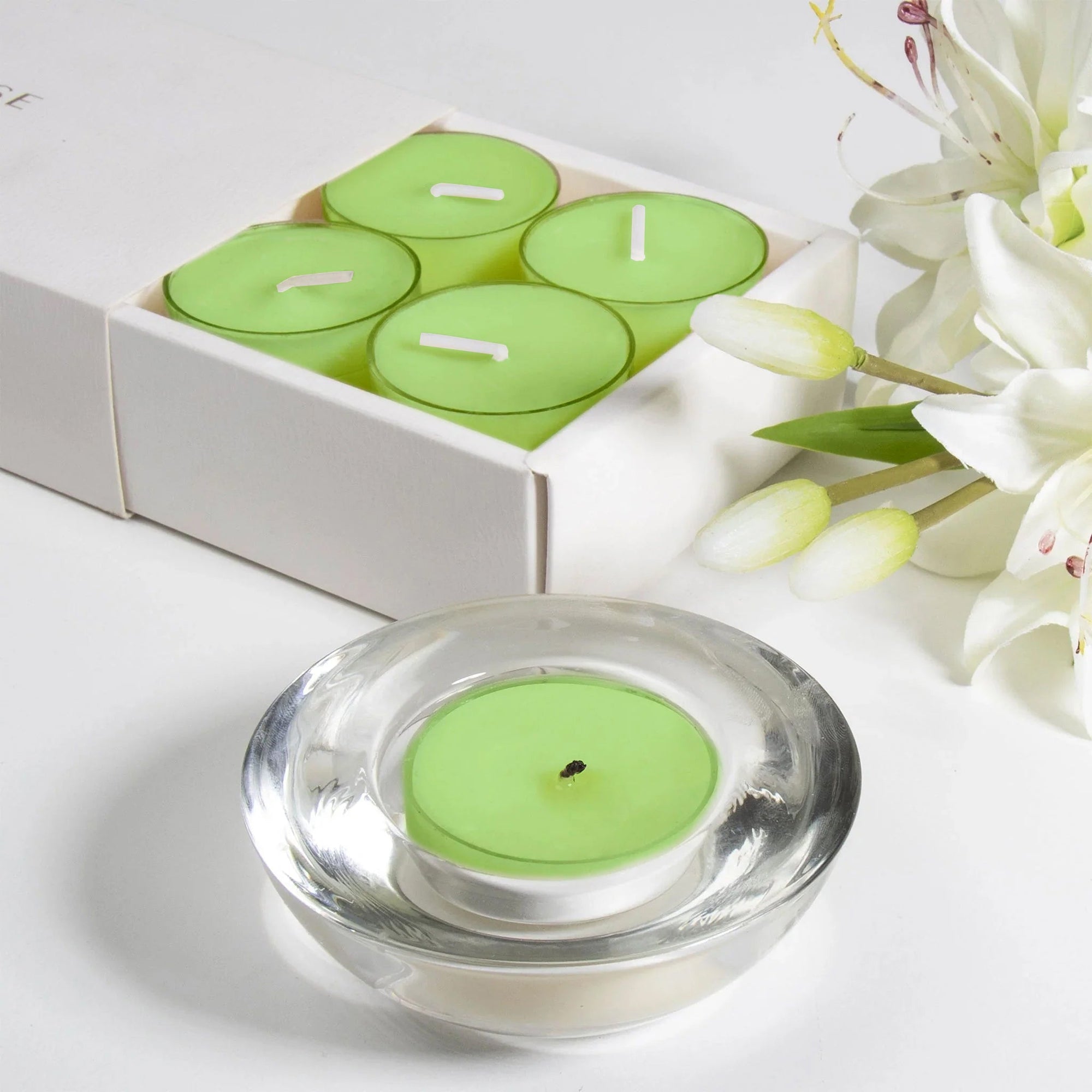 Close-up view of a green lily scented tealight candle sitting inside its heavy decorative glass holder, with the white gift box in the background.
