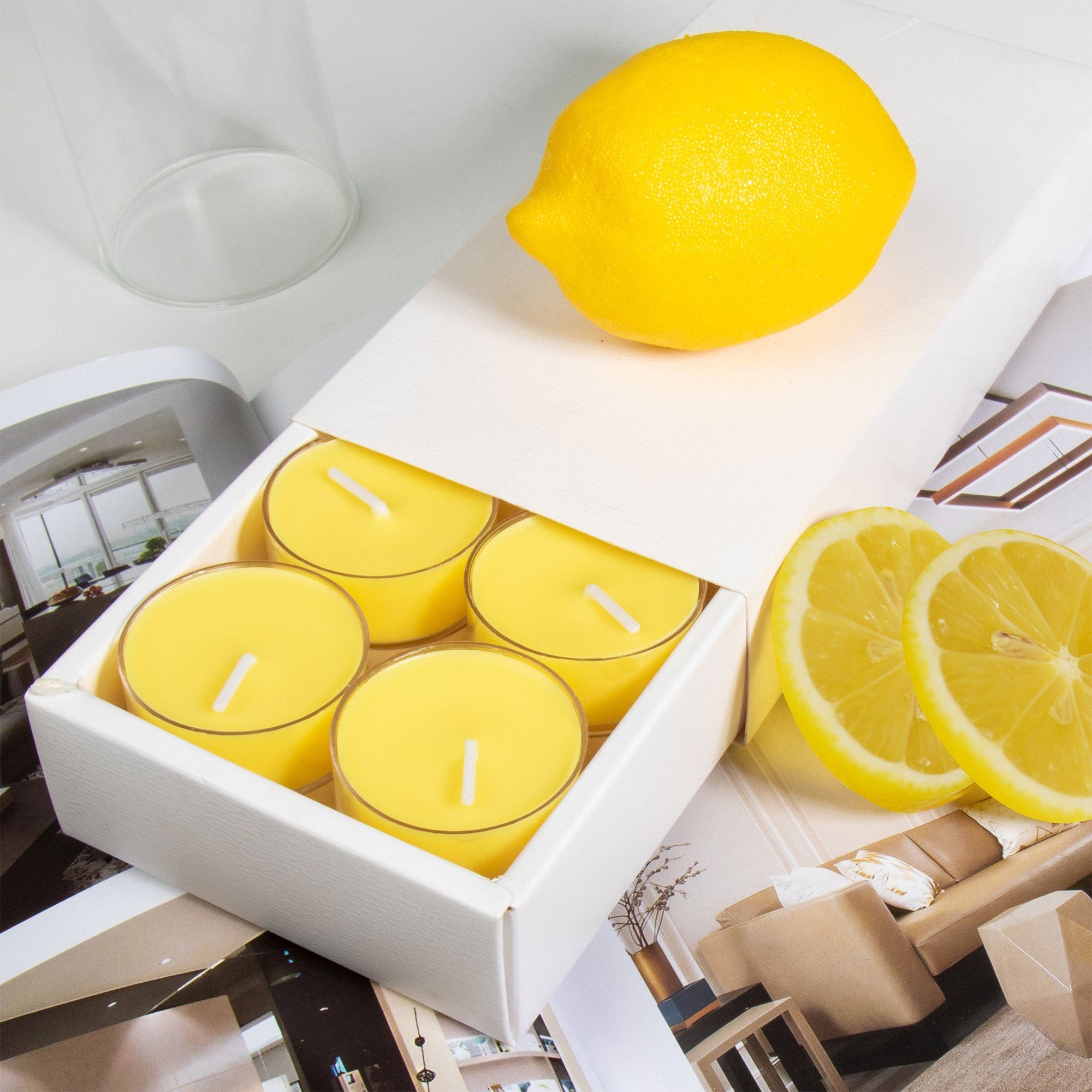 Close-up view of the premium white Vaucluse sliding packaging revealing a tiered 16-pack tray of yellow lemon scented tealight candles styled next to a whole lemon and fresh slices.