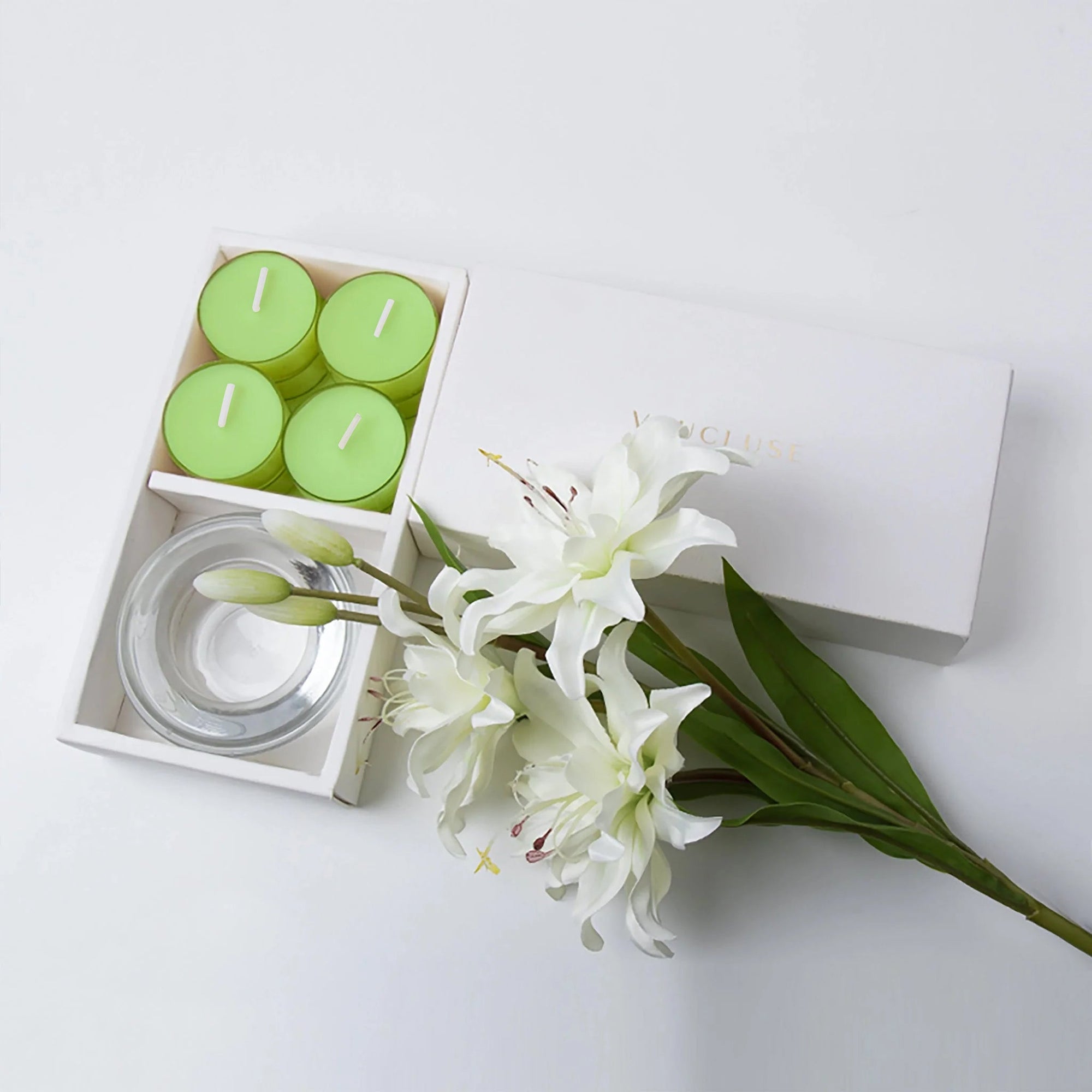 Minimalist top-down flat lay of the open green lily tealight candle set styled beautifully with fresh white lily flowers on a seamless white backdrop.