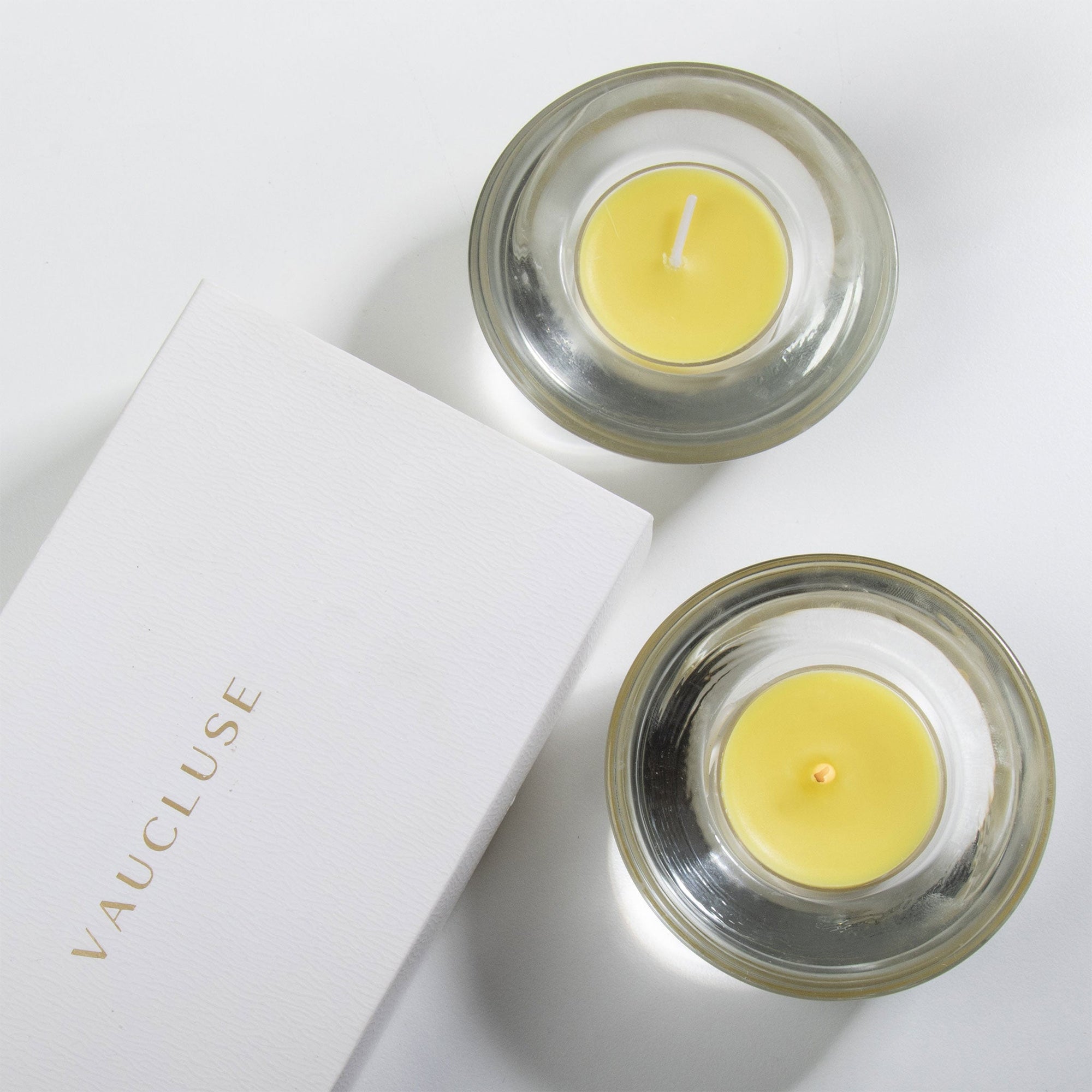 An overhead top-down view of yellow lemon scented tealight candles in clear glass holders next to a white Vaucluse luxury gift box.