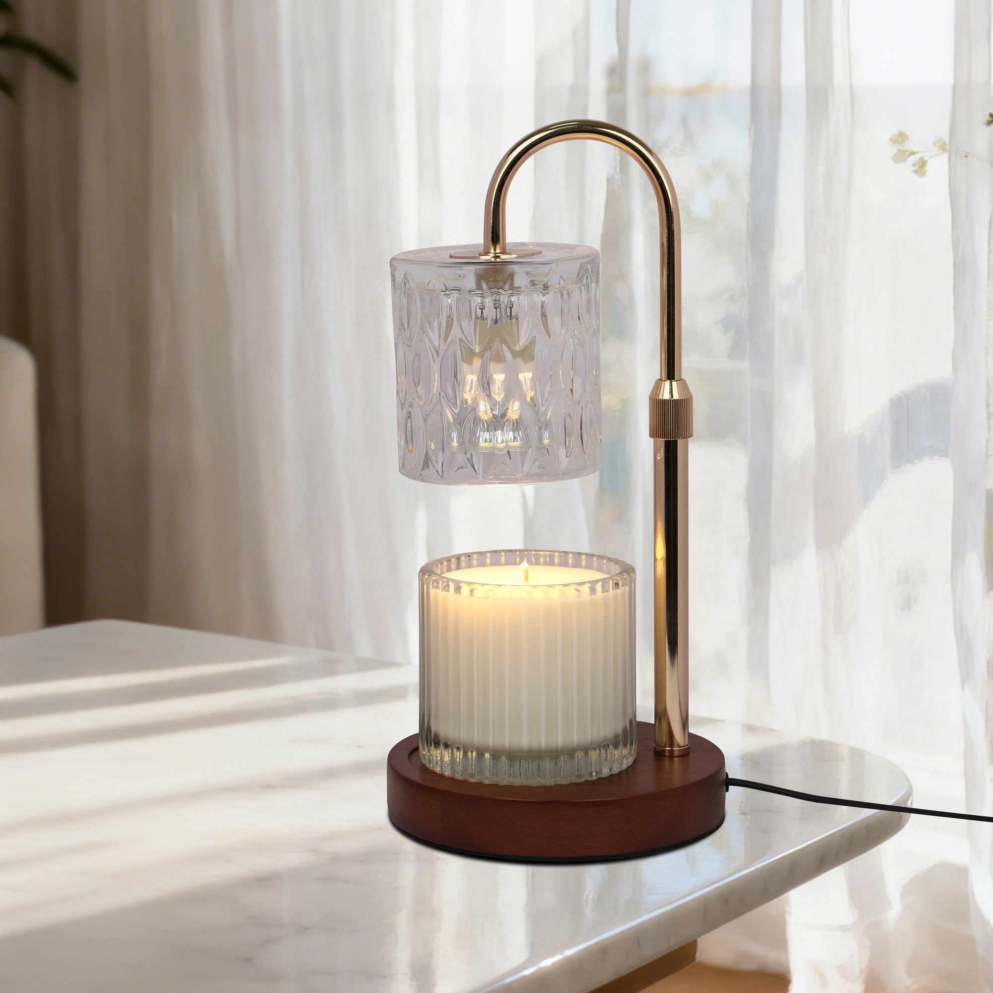 A lit transparent crystal candle warmer lamp casting a warm glow while melting a jar candle on a polished white marble tabletop.