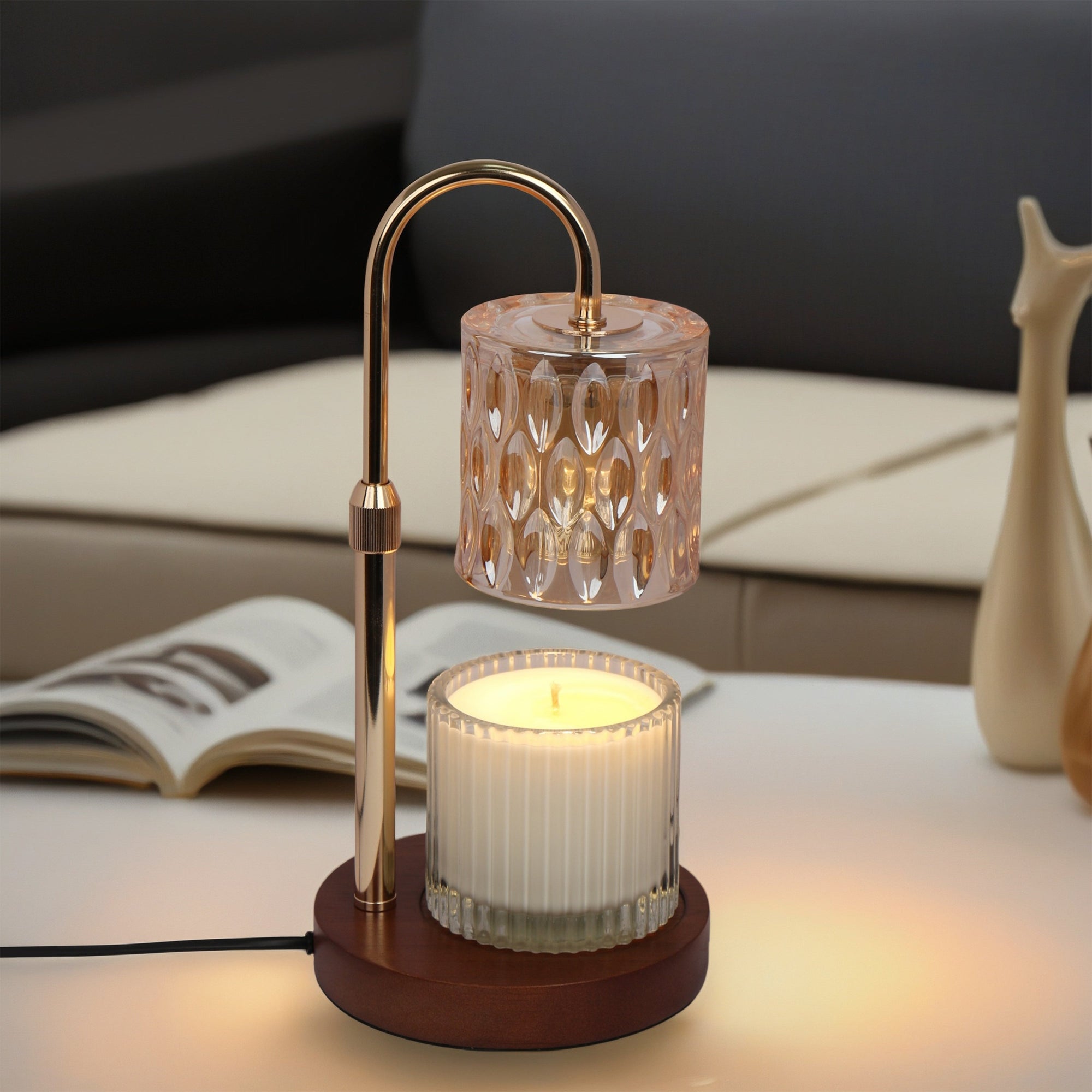 A lit crystal candle warmer lamp melting a scented jar candle on a coffee table with an open magazine and modern sofa in the background.