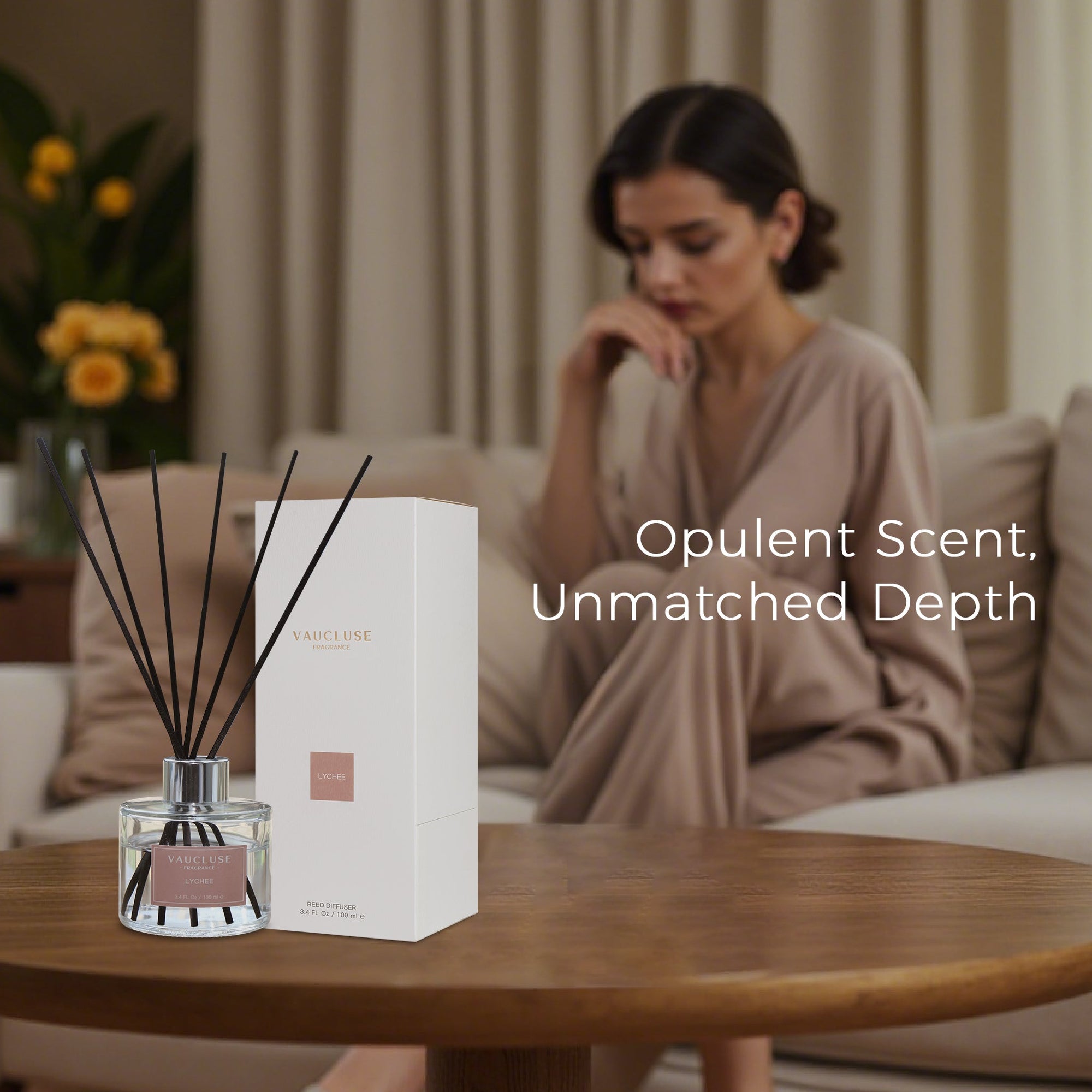A premium Vaucluse lychee reed diffuser and box set displayed on a wooden table, with a woman in a beige robe relaxing on a couch in a softly lit living room.
