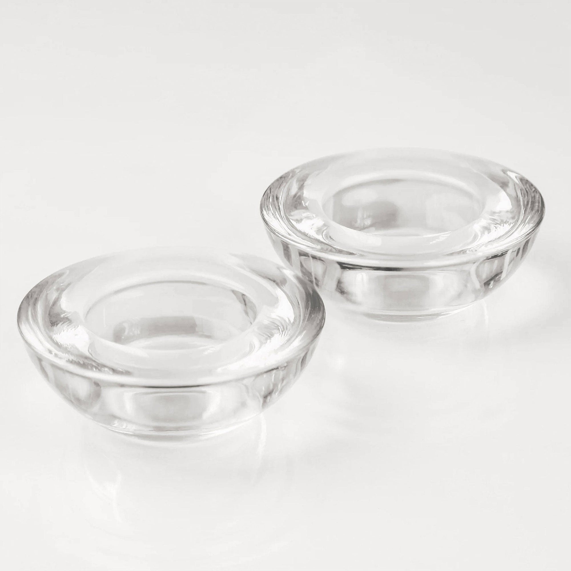 A close-up studio shot of two empty, thick clear glass tealight candle holders showcasing their heavy, high-quality round structure.