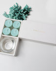 Minimalist overhead flat lay of the open aqua tealight candle set styled beautifully with a piece of decorative teal blue sea coral on a white surface.