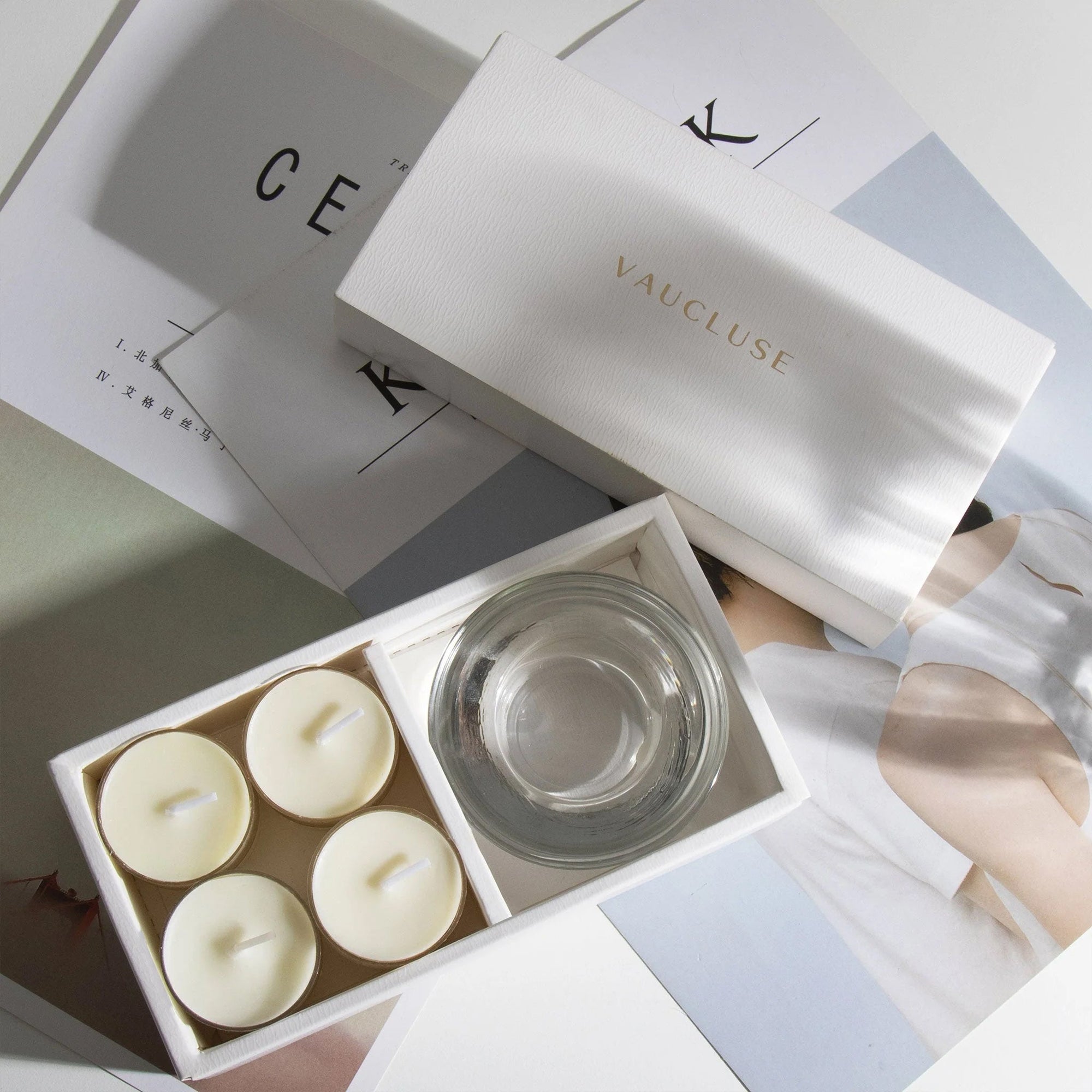 Aesthetic top-down view of the premium white musk scented tealight candle gift box arranged over editorial style design books and magazines.
