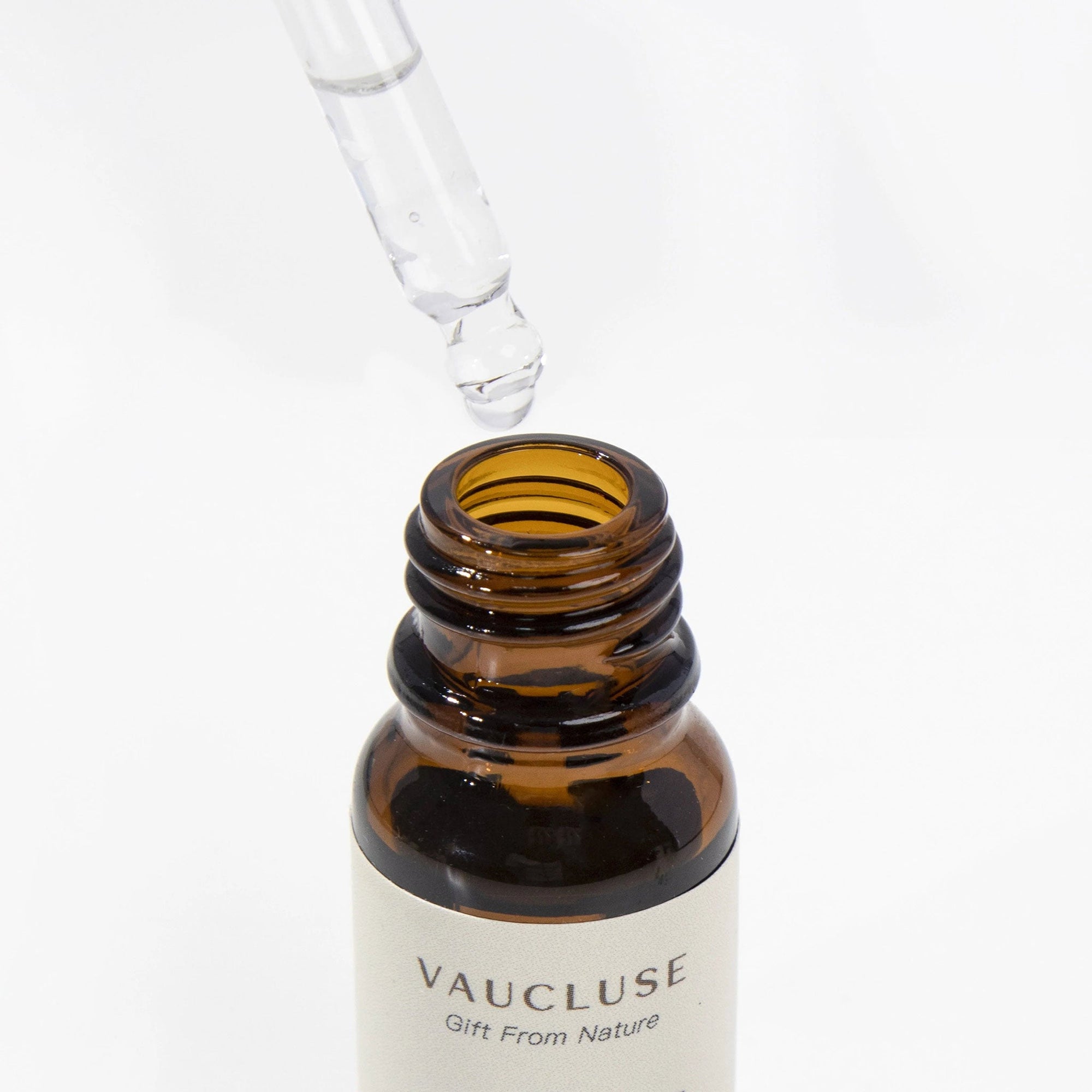 A clear glass pipette dropper dispensing a liquid drop into an open amber glass bottle of spring hyacinth essential oil.