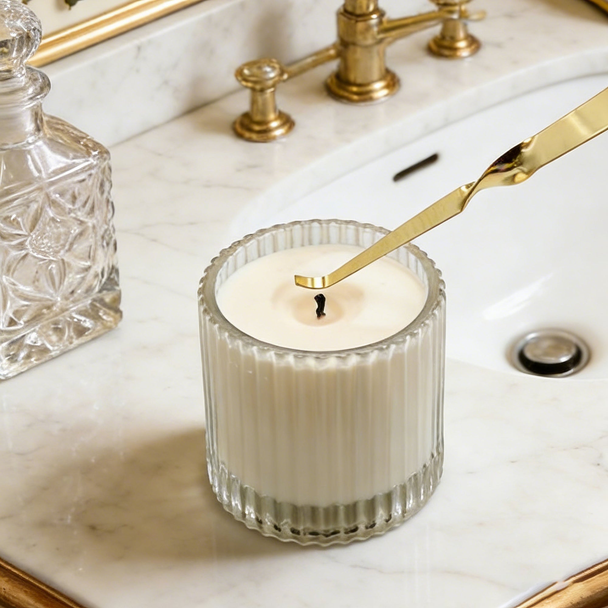 Adjusting a candle wick using a polished gold candle wick dipper inside a bathroom setting.