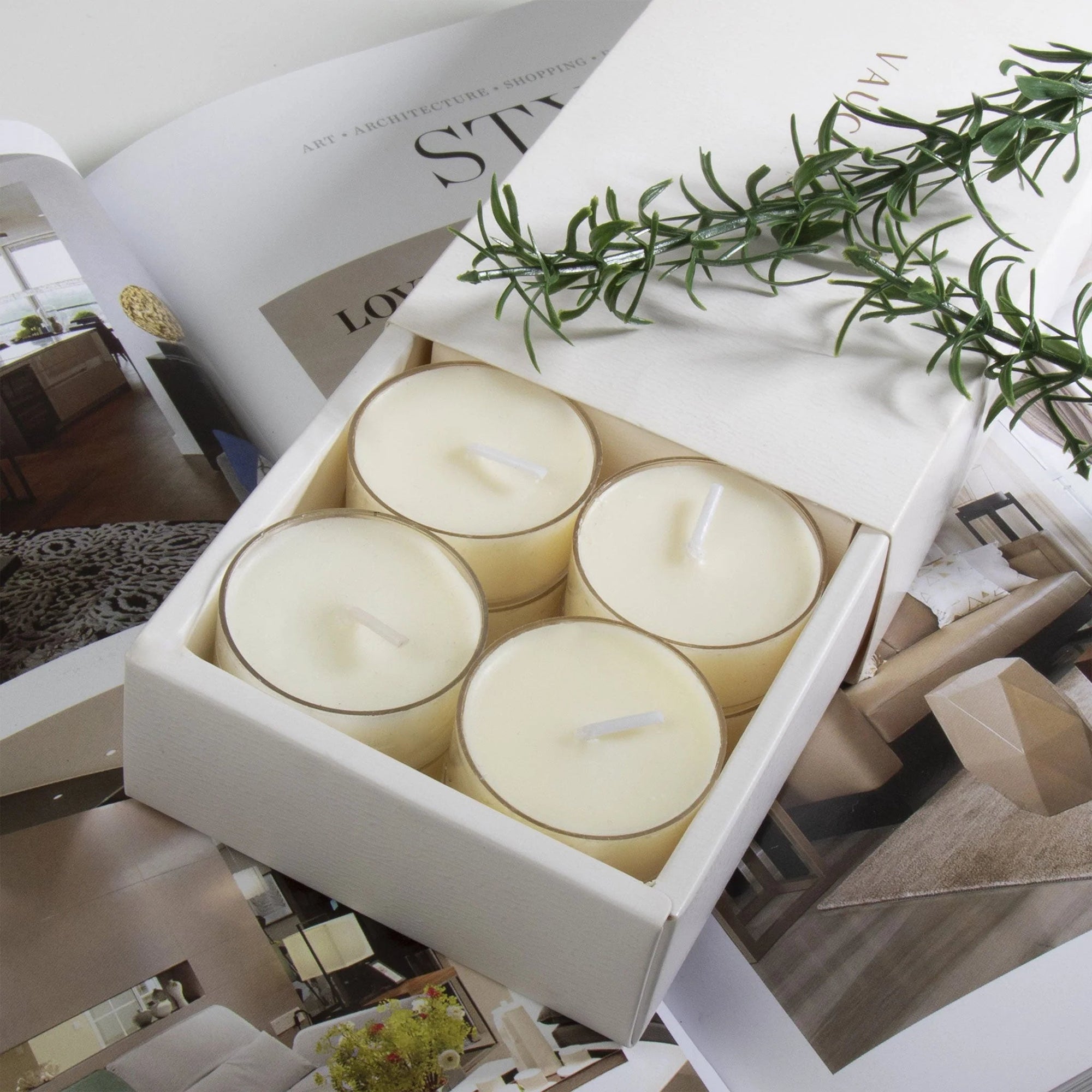 Close-up view of the premium white Vaucluse sliding packaging revealing a tiered 16-pack tray of vanilla scented tealight candles styled next to a fresh sprig of rosemary.