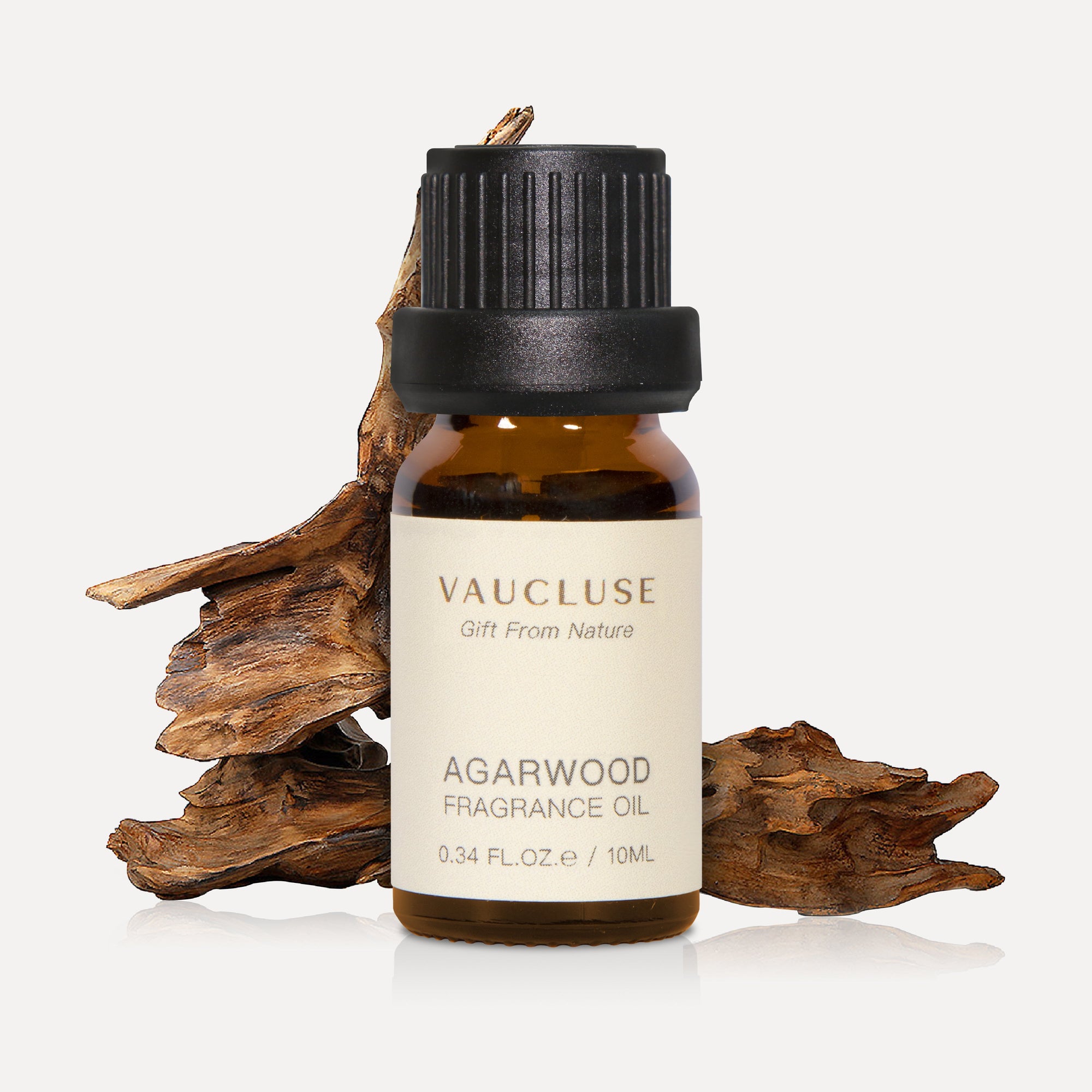 A 10ml amber glass bottle of Vaucluse Agarwood Essential Oil positioned in front of natural textured pieces of raw oud wood.