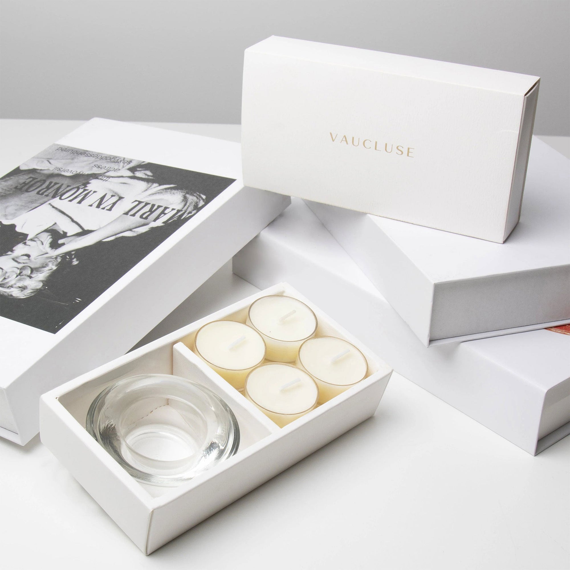Premium unboxing scene showing the open white jasmine candle holder set arranged next to stacked luxury gift boxes with gold branding.