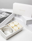 Premium unboxing scene showing the open white jasmine candle holder set arranged next to stacked luxury gift boxes with gold branding.
