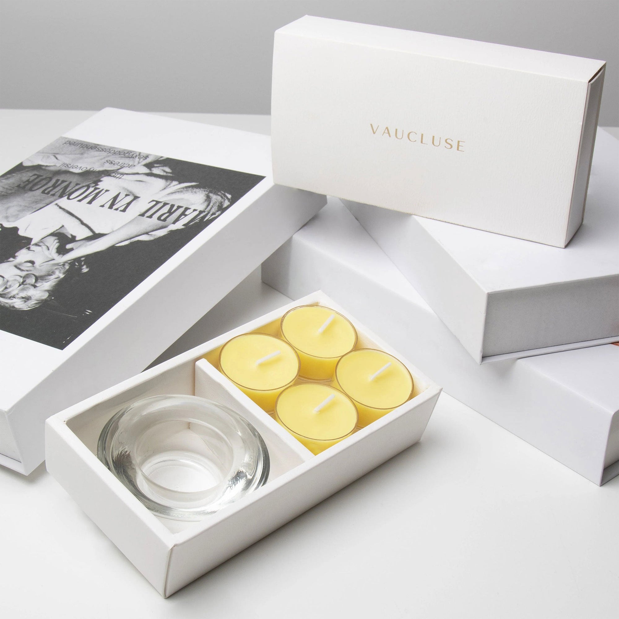 Premium retail unboxing display featuring the open yellow lemon tealight set resting against stacked white gift boxes with gold text.
