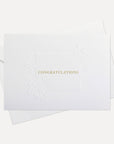 Front view of a minimalist luxury white congratulations card featuring elegant gold text and a blind-embossed floral border framework, displayed with its matching envelope.