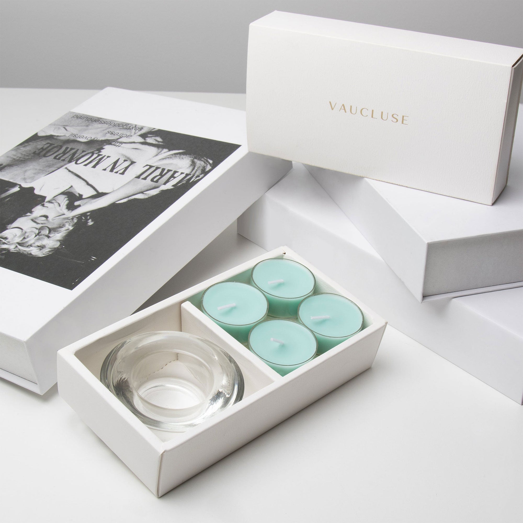 High-end unboxing presentation featuring the open ocean tealight candle set arranged with stacked white luxury gift boxes and an editorial book.