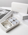 Luxury retail unboxing display showing the open grey velvet candle holder set resting against stacked premium gift boxes with gold branding.