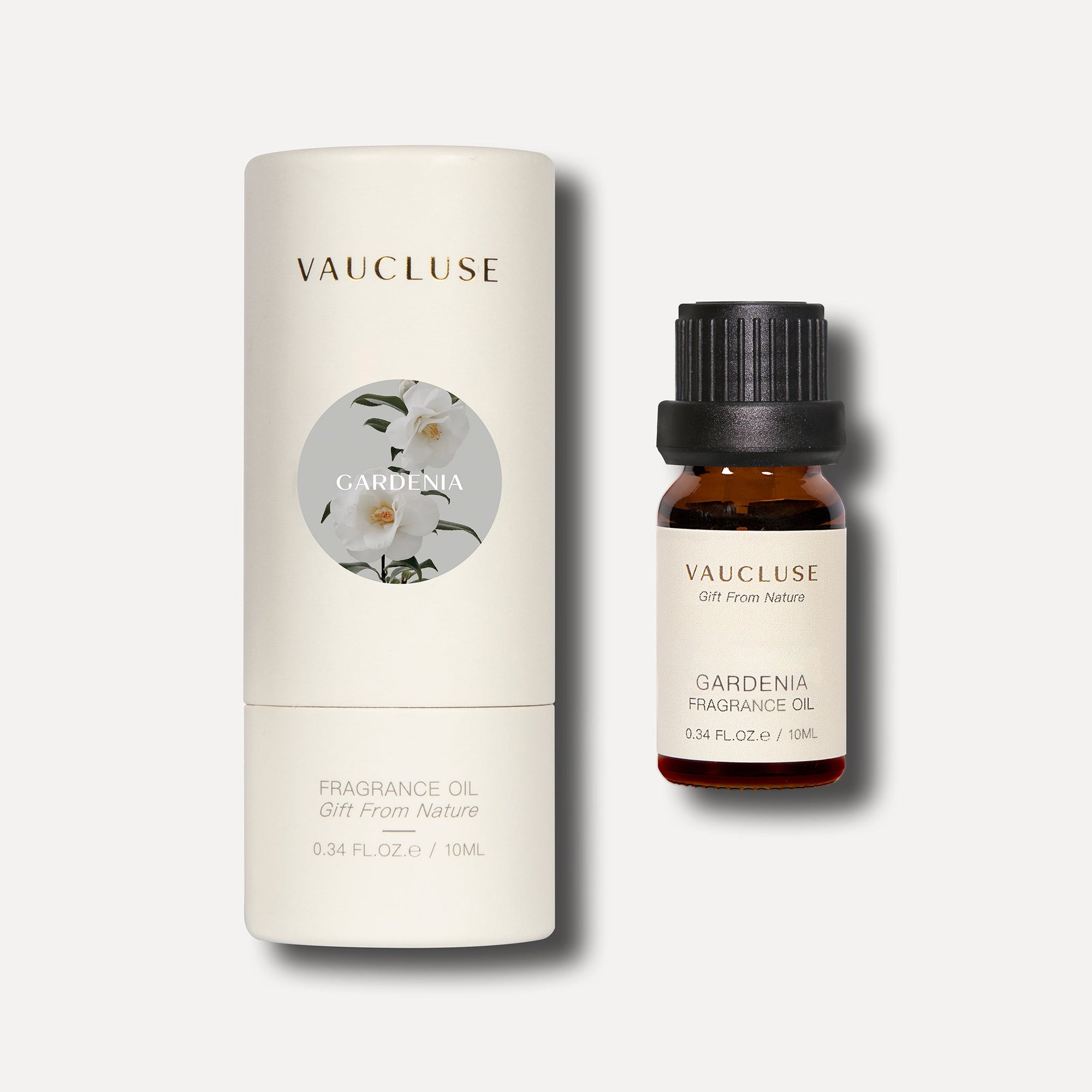 A 10ml bottle of Vaucluse gardenia essential oil standing next to its round white cylindrical container package.