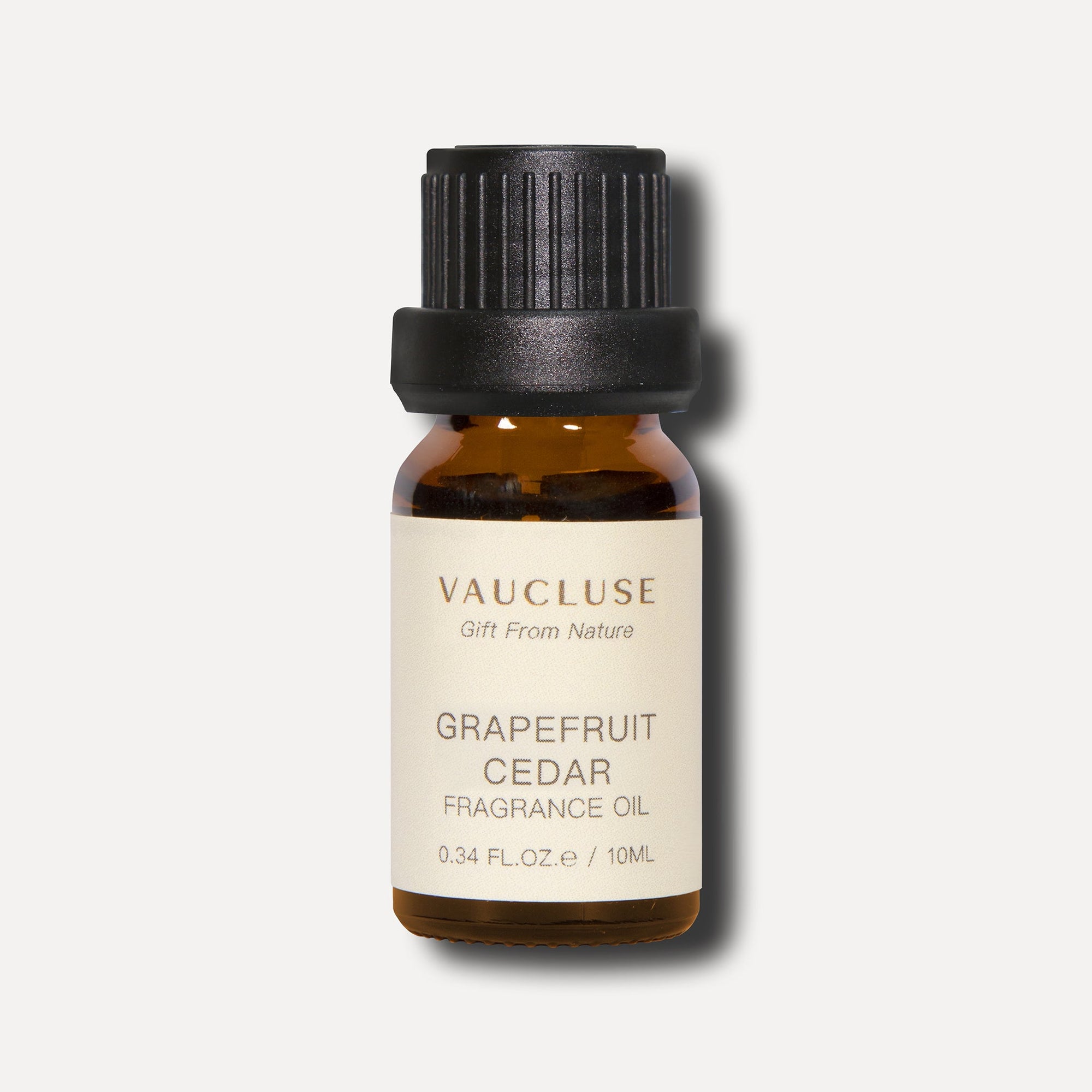 A minimalist studio front shot of a 10ml amber glass bottle of Vaucluse Grapefruit Cedar Essential Oil featuring a ribbed black cap.