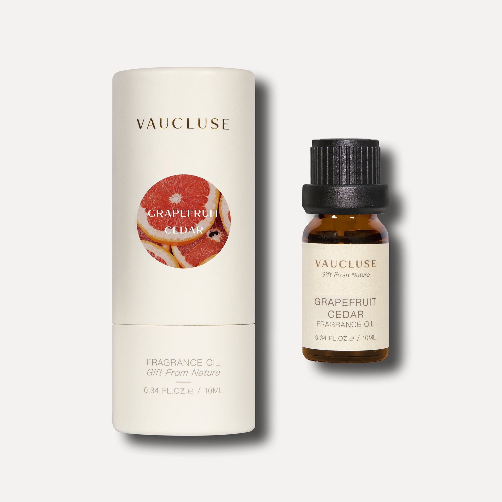 A 10ml amber bottle of Vaucluse grapefruit cedar fragrance oil sitting next to its white cylindrical packaging box.