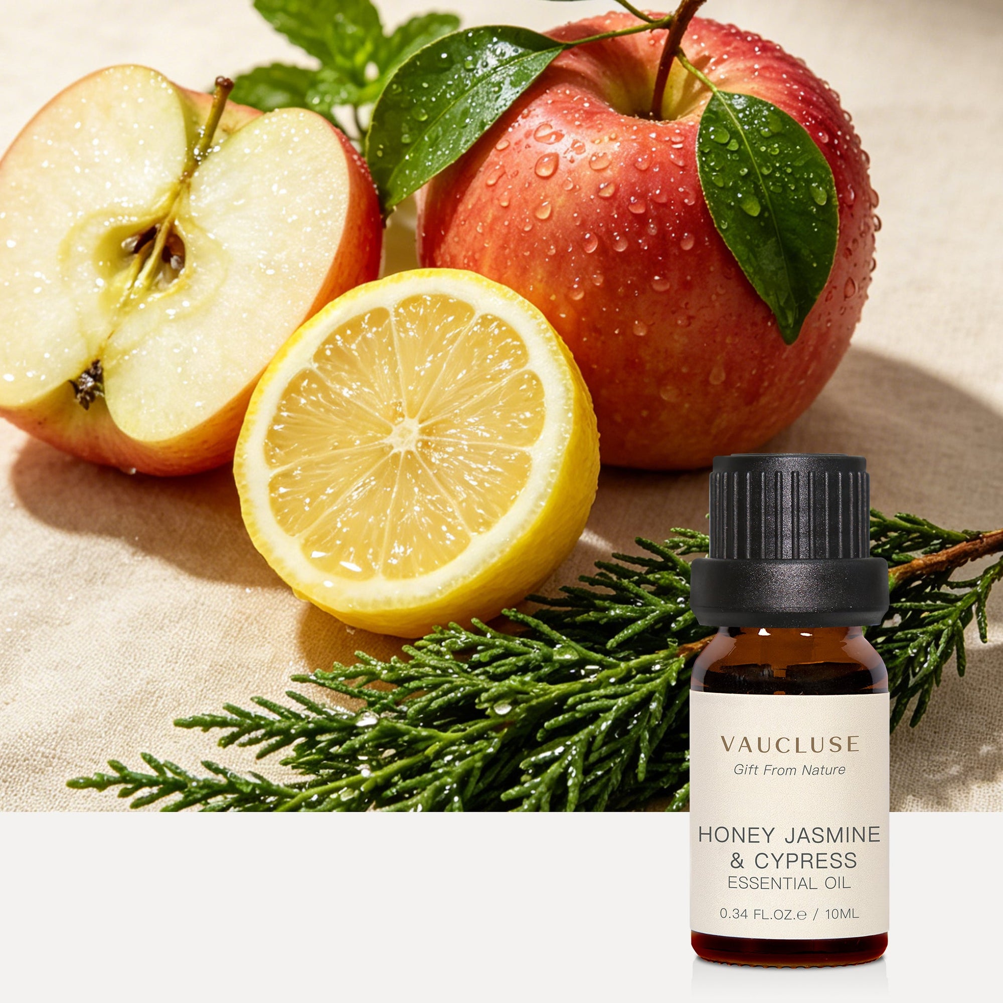 Vaucluse Honey Jasmine and Cypress essential oil bottle styled alongside sliced red apples, lemon halves, and green cypress branches.