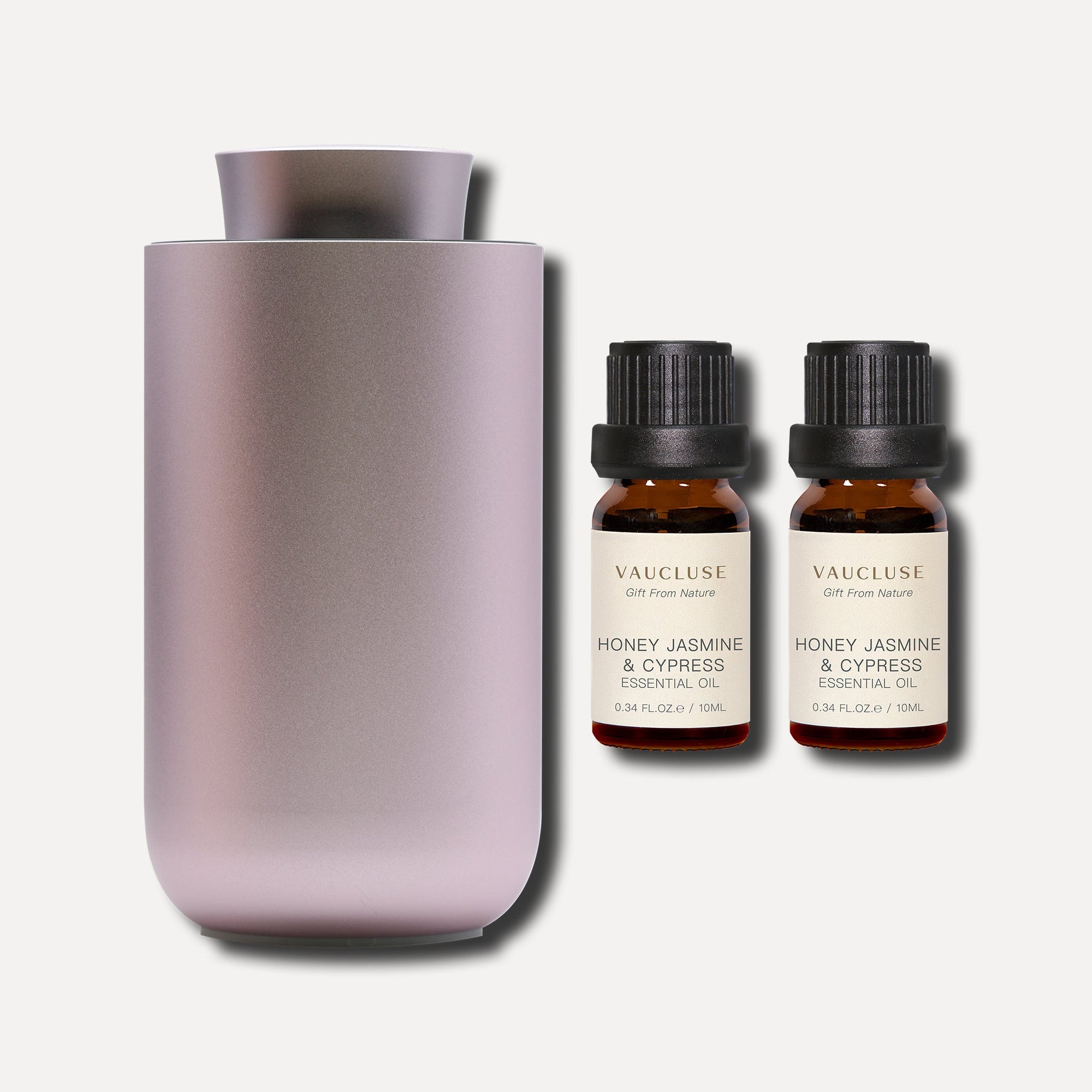 Two 10ml Vaucluse Honey Jasmine and Cypress essential oil amber bottles positioned next to a sleek metallic aroma diffuser.