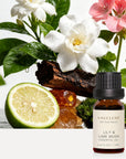 Vaucluse Lily and Lime Musk essential oil bottle styled with white gardenia flowers, sliced fresh lime, geranium, and bark.
