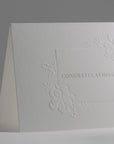 A detailed angle view showcasing the delicate blind-embossing technique and clean white paper stock used for the congratulations card.
