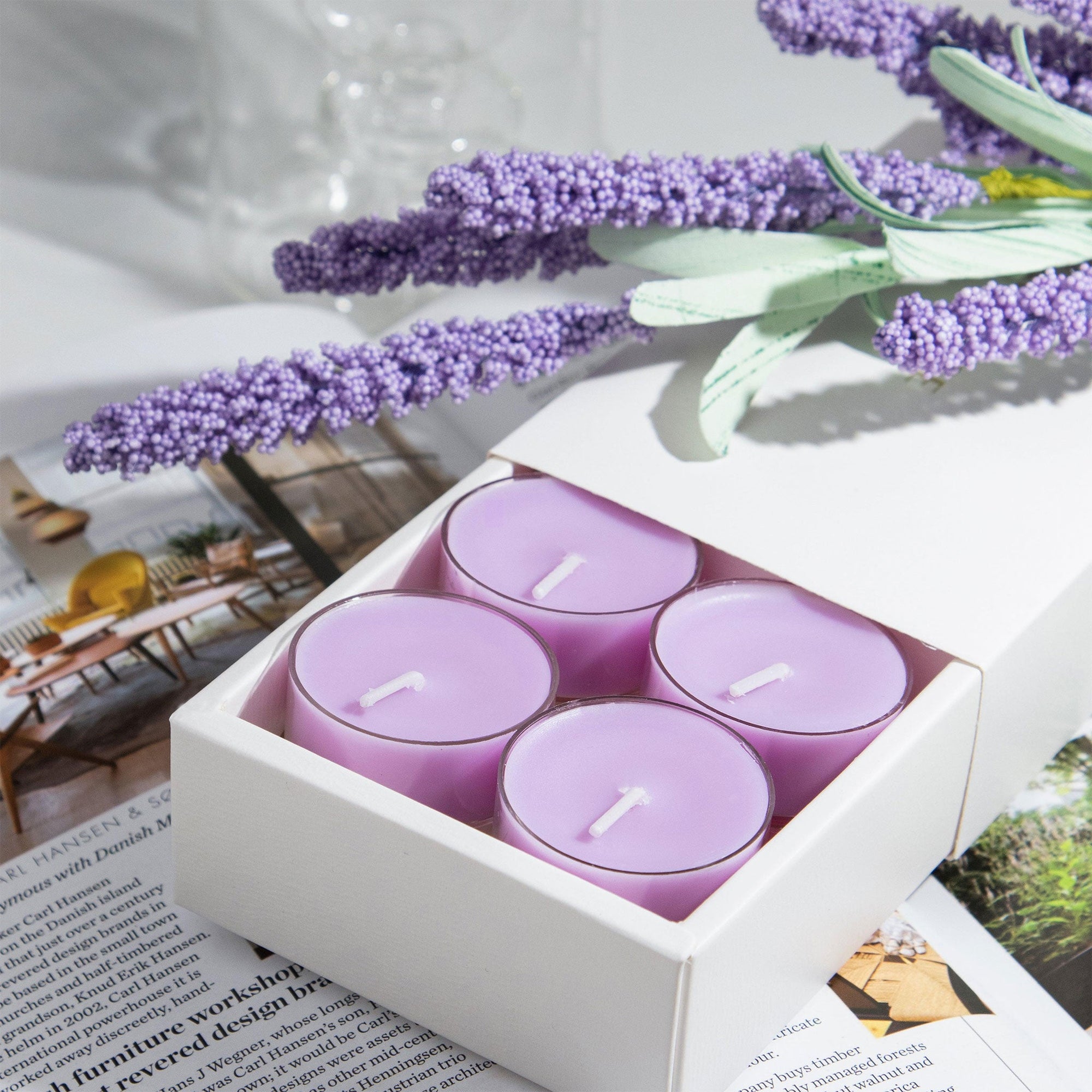 Close up lifestyle shot of a white gift box containing four purple Vaucluse Lavender soy tealights, styled on an open magazine with decorative lavender stems.