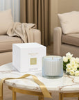 An unlit Vaucluse luxury scented candle sitting next to its elegant white and gold packaging box on a marble coffee table in a modern living room.