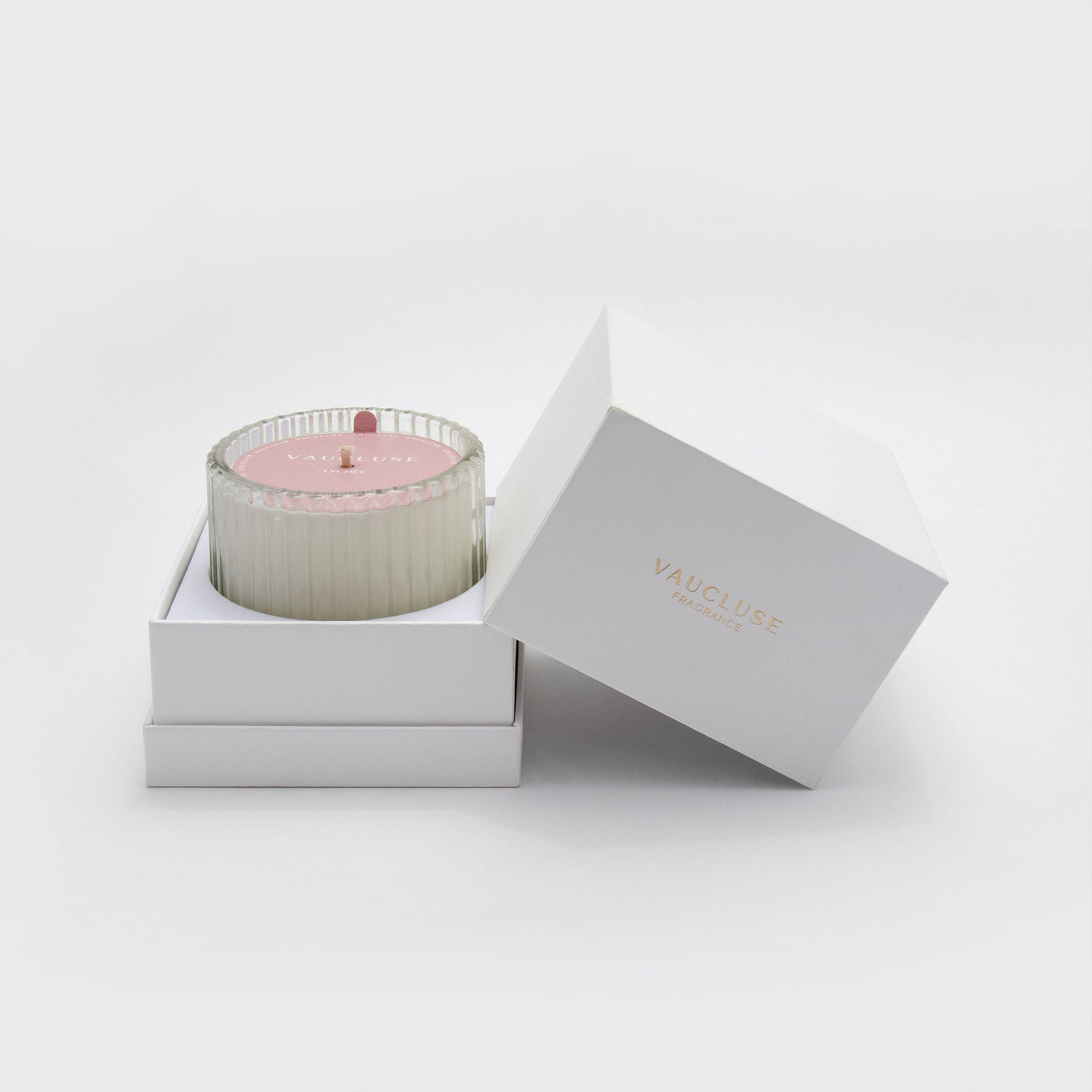A Vaucluse Lychee scented candle with pink lid resting inside its premium white two-piece gift box with the lid open.