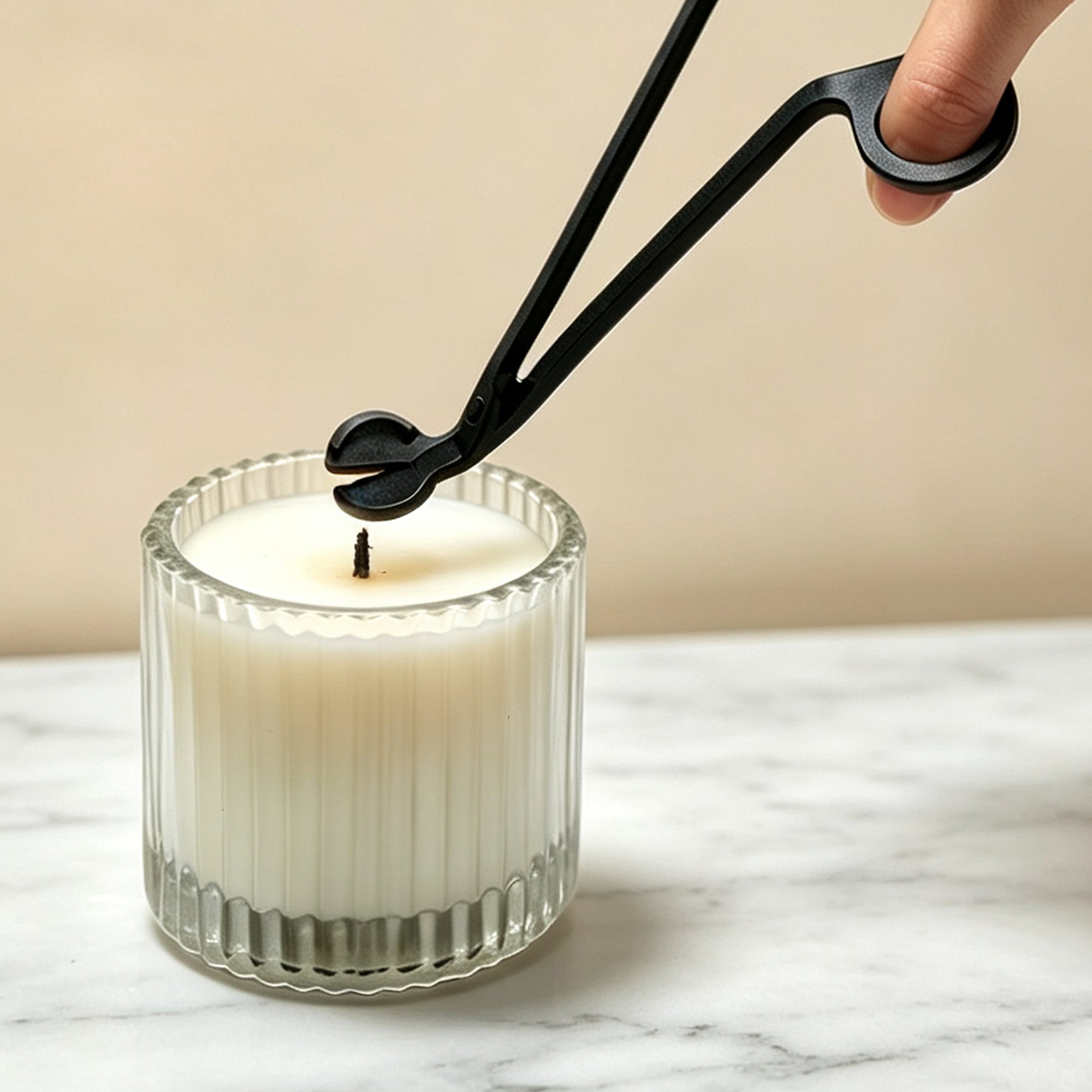 Trimming a candle wick with matte black wick trimmer scissors before lighting a luxury wax candle on a marble counter.