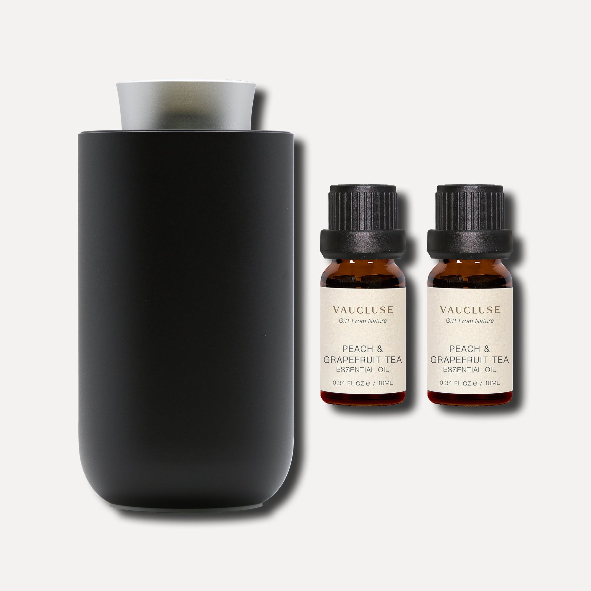 Two 10ml Vaucluse Peach and Grapefruit Tea essential oil bottles next to a matte black aroma diffuser.