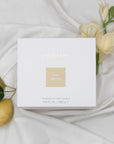 Top view of the minimalist white Vaucluse Pear & Freesia scented wax candle packaging box, decorated with delicate white flowers and fresh pears on a soft silk backdrop.