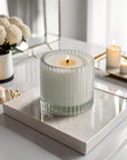 A lit Vaucluse Pear & Freesia luxury scented candle in a ribbed glass jar, placed on a white marble tray in a bright, modern room.