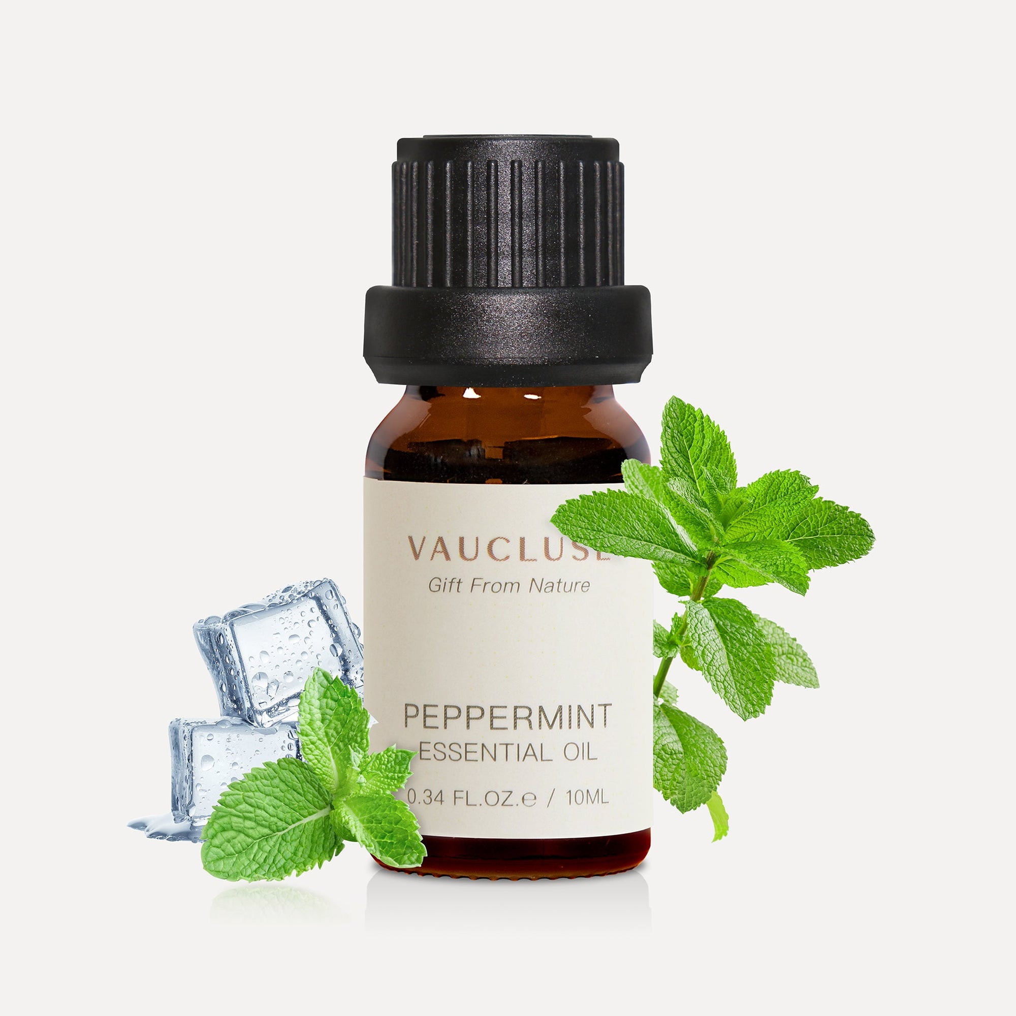 A 10ml amber glass bottle of Vaucluse Peppermint Essential Oil styled with fresh green mint leaves and clear ice cubes to emphasize a crisp, cooling aroma.