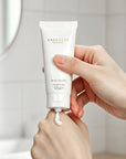 Woman squeezing a dollop of Vaucluse Rose Velvet hand cream onto the back of her hand in a brightly lit bathroom.