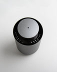 A high-angle top-down view of the circular gun metal waterless diffuser highlighting the central scent mist nozzle and clean interface.